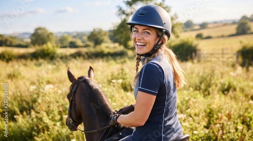 Woman equestrian wearing helmet riding horse in field. Happy jockey enjoying outdoor sport activity in countryside. Lifestyle hobby, animal care and active leisure in rural nature at summer.
