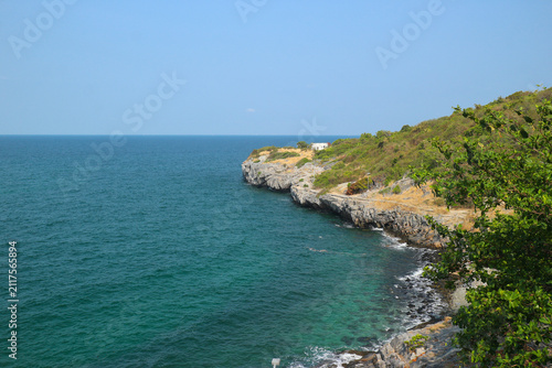 Breathtaking rocky coastline of Koh Sichang island in Thailand featuring crystal clear blue ocean waters and lush green hills under a bright summer sky for travel campaigns.