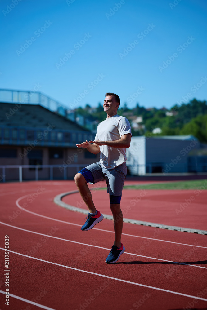 Fototapeta premium Smiling male runner warming up with high knees on outdoor track