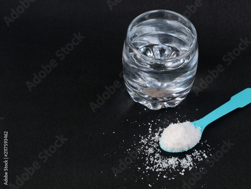 Foto A glass of saltwater solution with blue spoon filled with sea salt crystals on a