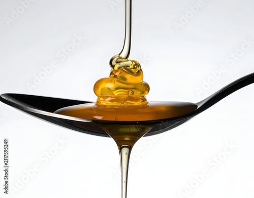 Golden Honey Pouring onto a Black Spoon Isolated on a White Background