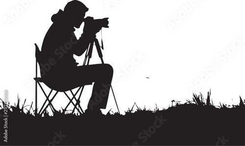 Black silhouette of a photographer sitting in a folding chair taking a white