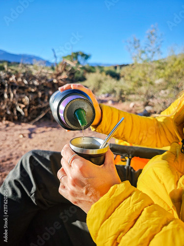 Woman drinking traditional yerba mate tea while camping in countryside during sunny day