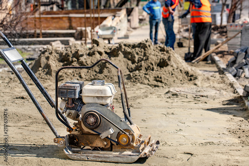 Construction workers use compactor during building project at construction site in daytime.
