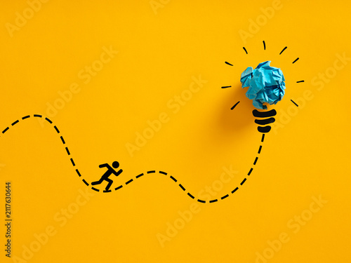 Person running an erratic path towards a crumpled paper lightbulb idea. Pursuing creative ideas.
