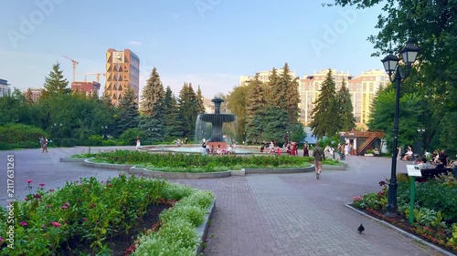  Park scene with fountain surrounded by flowers and people enjoying leisure time in a vibrant urban setting during sunny weather
