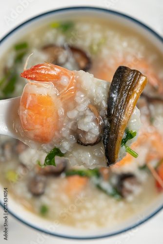 Spoonful of seafood congee with shrimp, eel and mushrooms above a ceramic bowl
