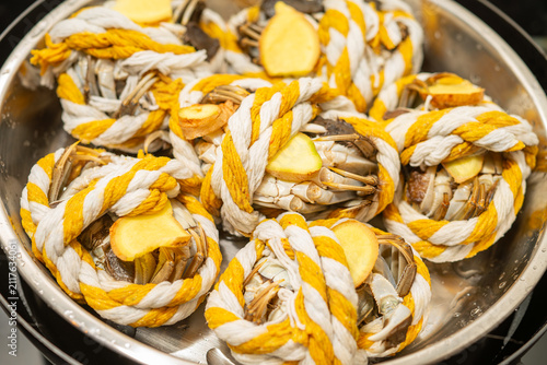Hairy crabs bound with striped rope and ginger slices placed inside stainless steel steamer pot