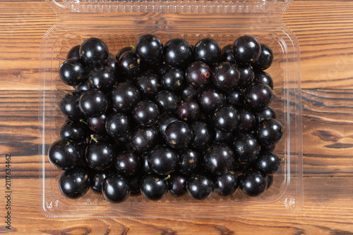Fresh jabuticaba fruits densely packed inside a transparent plastic clamshell container on wooden planks