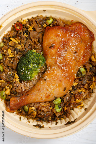 Roasted chicken leg over mixed vegetable fried rice served in disposable lunch bowl