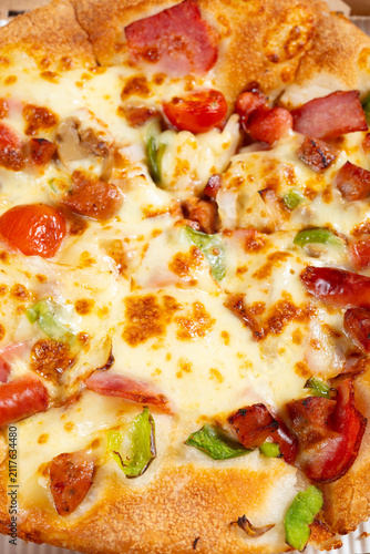 Luxury supreme pizza topped with melted cheese, ham, sausages, cherry tomatoes and bell peppers
