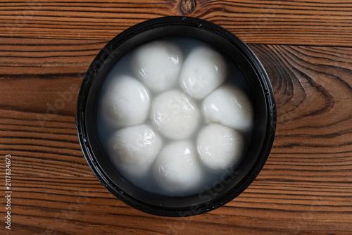 Glutinous rice tangyuan soaking in clear water inside a black plastic bowl on wooden planks