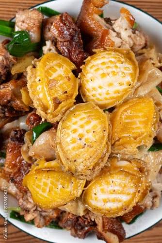 Braised abalone mixed with roasted meat, green scallions and yuba served on a white ceramic plate