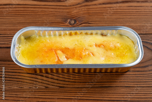 Baked cheese custard dessert resting inside a rectangular aluminum foil tray on wooden table