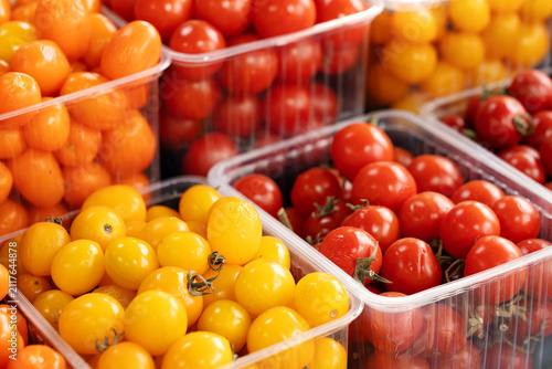 Cuadro en lienzo Assorted fresh red, orange, and yellow cherry tomatoes packaged in clear plastic containers for sale at a local farm market