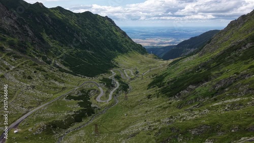 Forward drone flight following the spectacular Transfăgărășan highway beneath dramatic clouds with towering mountains and distant valleys creating an iconic Romanian landscape.