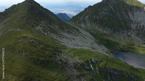 Forward aerial drone flight between dramatic mountain peaks revealing distant valleys and expansive alpine scenery in Romania's Făgăraș Mountains.