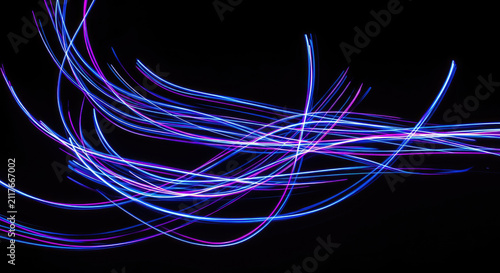 A long-exposure photograph captures streaks of vibrant light, primarily purple and blue, creating an abstract, flowing pattern against a stark black background.