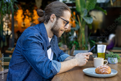 Принти на полотні Bearded young caucasian man with a phone in a cafe