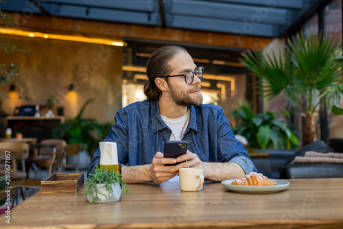Foto Young bearded man in eyeglasses sitting at the table in a cafe