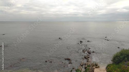 A serene, overcast ocean vista featuring rocky formations along the coastline, evoking a sense of calm solitude and natural beauty. Nobody, no people, ideal for travel or mindfulness themes.