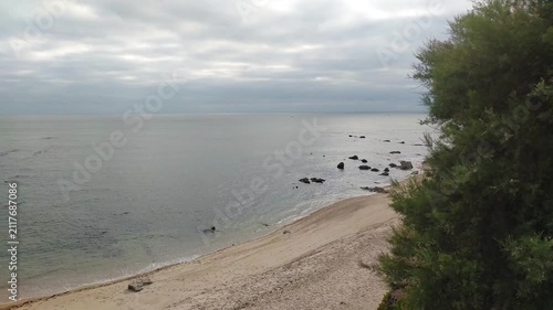 A tranquil, overcast coastal landscape featuring a sandy beach, calm ocean, and rugged rocks under a soft sky. Nobody is present in this peaceful, meditative scene, perfect for travel concepts.