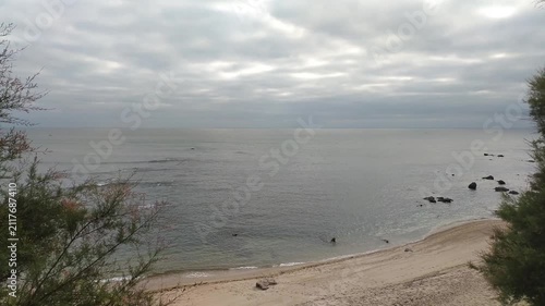 A peaceful, overcast seaside view from a coastal cliff, framing a calm ocean and sandy beach. No people in this moody, tranquil landscape perfect for nature travel themes and contemplative moods.
