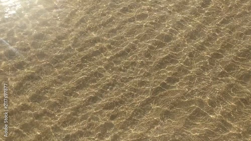 Clear, sundrenched water ripples over a textured sandy seabed, creating a serene, meditative atmosphere. This peaceful, nobody scene evokes tranquility, perfect for nature and wellness themes.