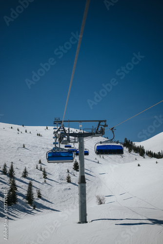 Photography A row of blue chairlift cabins ascends a snow-covered mountain slope with scattered evergreen trees