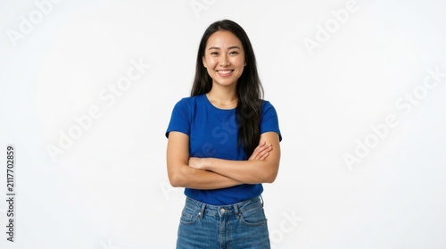 Happy young asian woman wearing a blue t-shirt and jeans standing with her arms crossed looking at the camera smiling