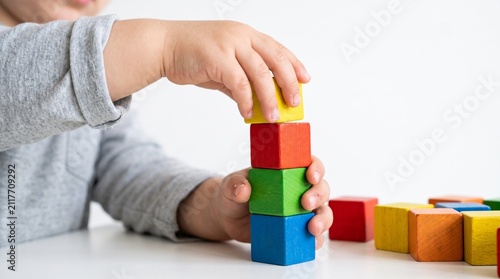 Close-up of a child's hands stacking colorful wooden blocks on a white table