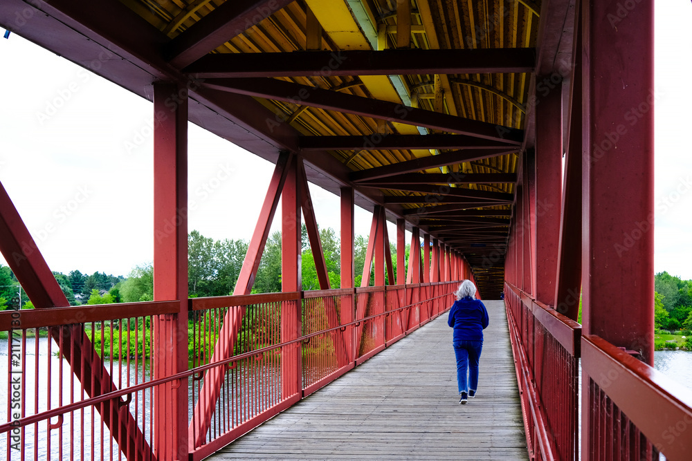 Obraz premium Passerelle piétonne à l'île Pozer, à Saint-Georges-de-Beauce, Québec. Pont en bois rouge enjambant la rivière.