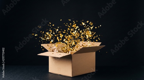Cardboard box exploding with golden confetti against a dark background