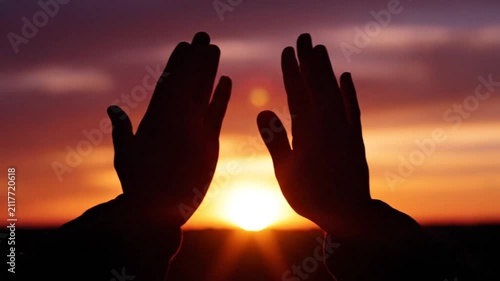 Silhouette of hands raised toward a colorful sunset sky