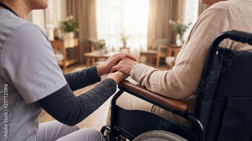 Caregiver providing comfort to senior patient sitting in wheelchair at home
