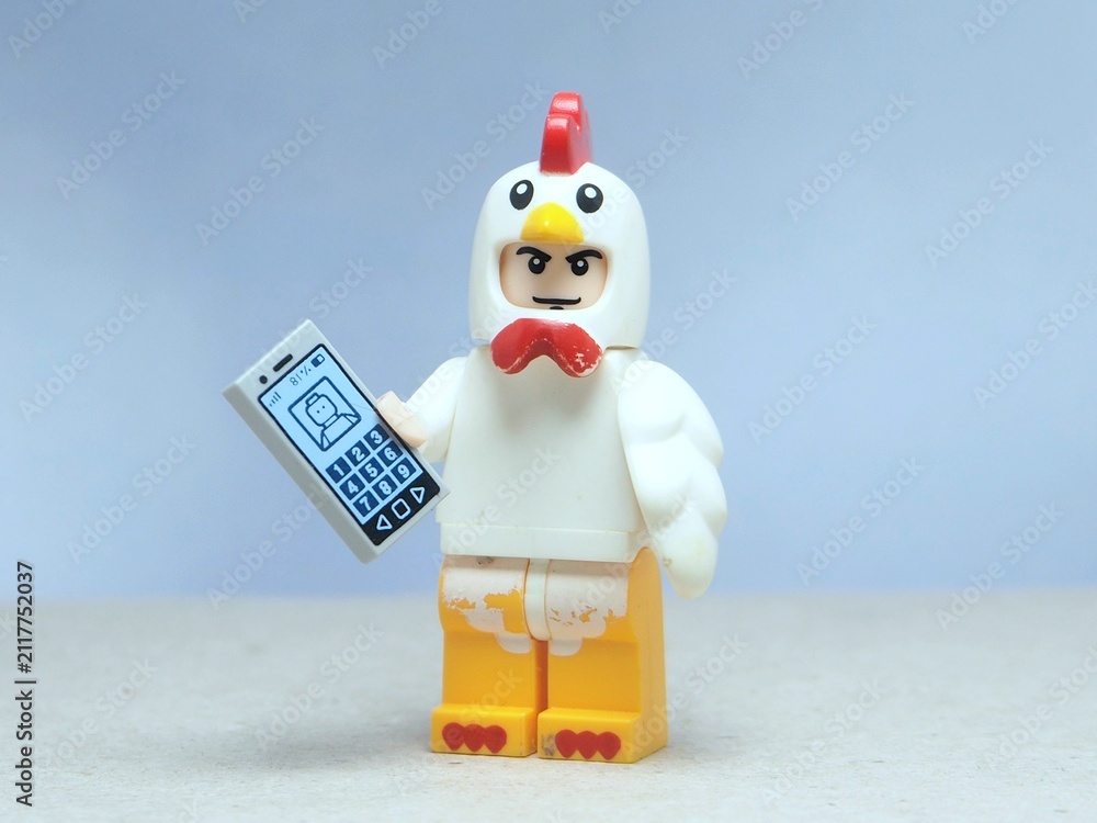 Naklejka premium Indonesia - May 16, 2025 : Mini toy of action figure at table with blurred background. Miniature photography concept design. Minifigure of chicken character hold smartphone on hand. Smart farm concept