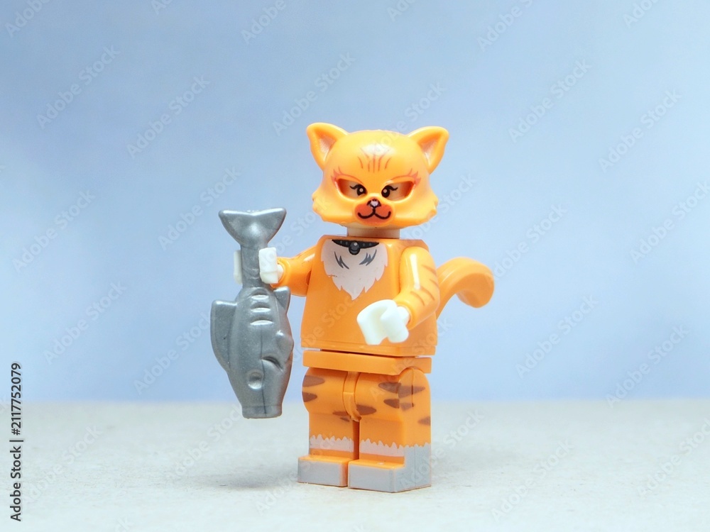 Fototapeta premium Indonesia - May 16, 2025 : Mini toy of action figure at table with blurred background. Miniature photography concept design. Minifigure of orange cat character hold the fresh fish.