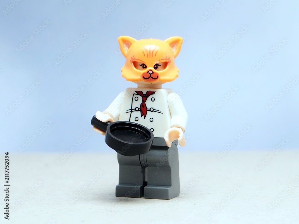 Fototapeta premium Indonesia - May 16, 2025 : Mini toy of action figure at table with blurred background. Miniature photography concept design. Minifigure of orange cat character wearing chef costume with pan and fish.