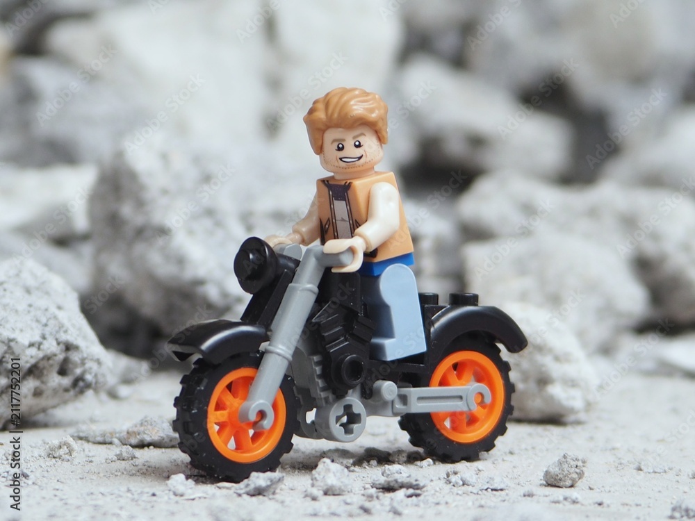 Fototapeta premium Indonesia - May 8, 2025 : Mini toy of action figure at table with blur background. Miniature photography concept design. Traveling man with his motorcycle and sunglasses. Touring at outdoor concept.