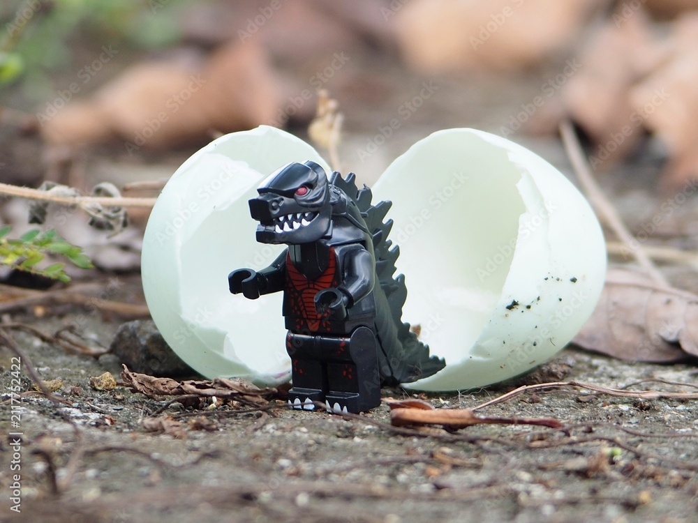 Fototapeta premium Indonesia - May 3, 2025 : Mini toy of action figure at outdoor with blurred background. Wild photography concept design. Minifigure of Baby Godzilla character coming out from egg. New born concept