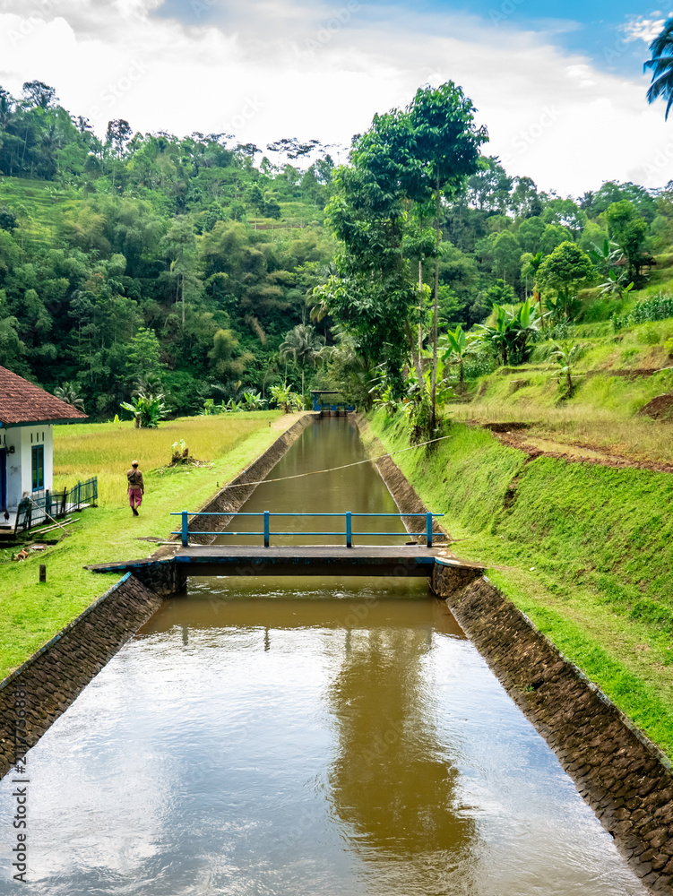 Fototapeta premium Peaceful Irrigation Canal with Small Bridge in Mountain Countryside 