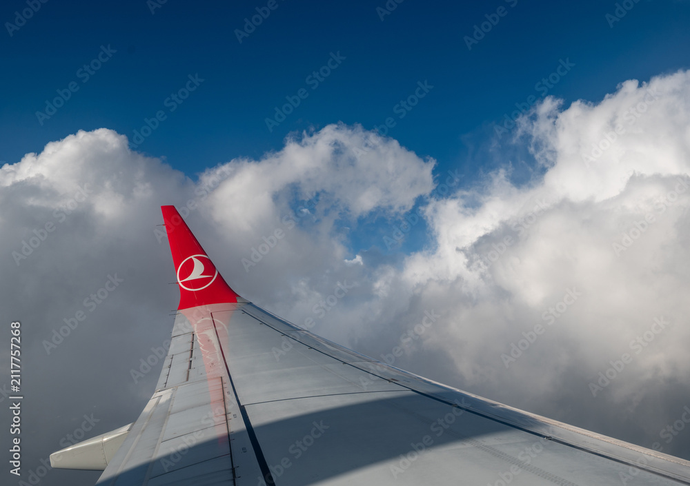 Obraz premium Caselle airport, turin province, italy. August 1, 2025. Turkish airlines aircraft wing flying over caselle airport, turin, italy. Experiencing travel, aviation, and clear blue sky with white clouds