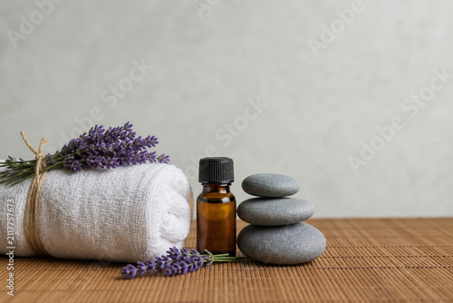 Spa essentials with rolled towel, lavender, grey stones and amber oil bottle on bamboo mat, wellness concept.