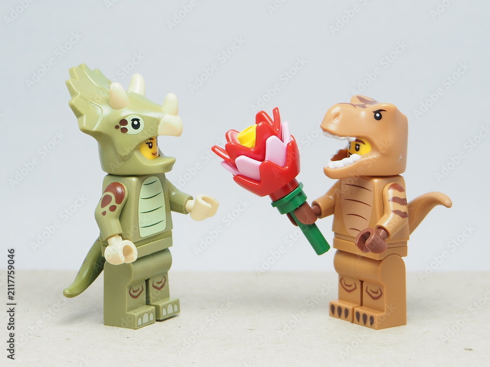 Fototapeta premium Indonesia - March 4, 2026 : Mini toy of action figure at outdoor with blur background. Miniature photography concept design. Minifigure of T-rex Dino character give bouquet of flower to triceratops.