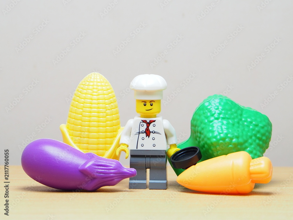 Fototapeta premium Indonesia - February 10, 2026 : Mini toy of action figure at outdoor with blur background. Miniature photography concept design. Minifigure of chef character with eggplant, corn, broccoli and carrot.