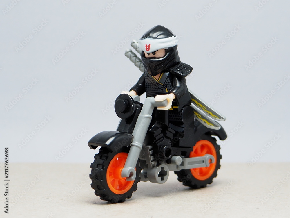 Fototapeta premium Indonesia - December 1, 2025 : Mini toy of action figure at outdoor with blurred background. Miniature photography concept design. Minifigure of Ninja Go character riding the motorcycle at road.