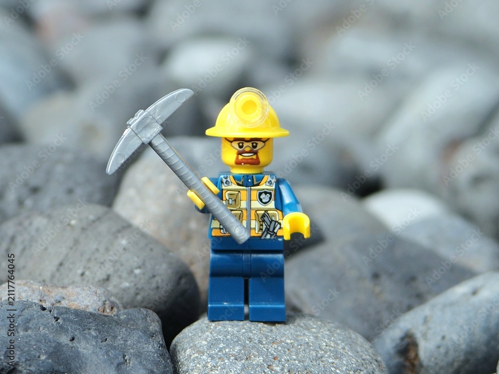 Fototapeta premium Indonesia - November 30, 2025 : Mini toy of action figure at outdoor with blurred background. Miniature photography concept design. Minifigure of miner worker at rock mountain with pickaxe and helmet.
