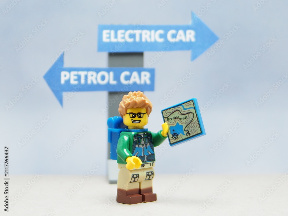 Fototapeta premium Indonesia - April 14, 2025 : Mini toy of action figure at table with blurred background. Auto photography concept design. Minifigure of people character with roadsign. Electrical EV Car vs Petrol Car.