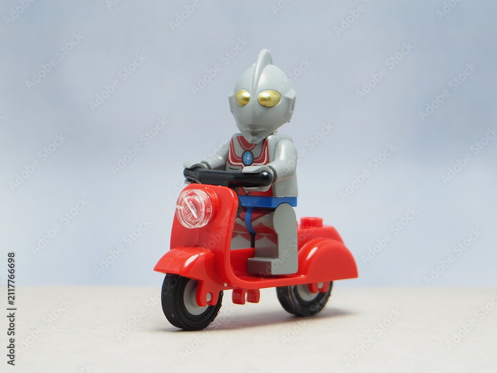 Obraz premium Indonesia - April 14, 2025 : Mini toy of action figure at outdoor with blur background. Miniature photography concept design. Minifigure of Ultra Man character from fiction film. Riding the scooter.