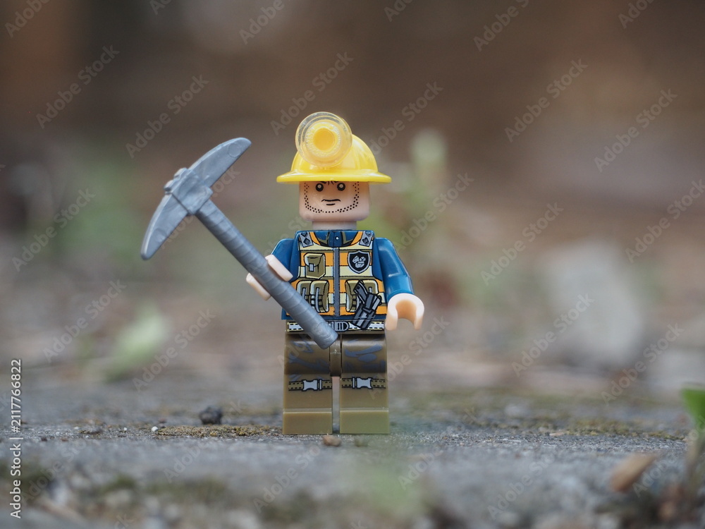 Fototapeta premium Indonesia - November 30, 2025 : Mini toy of action figure at outdoor with blurred background. Miniature photography concept design. Minifigure of miner worker at rock mountain with pickaxe and helmet.